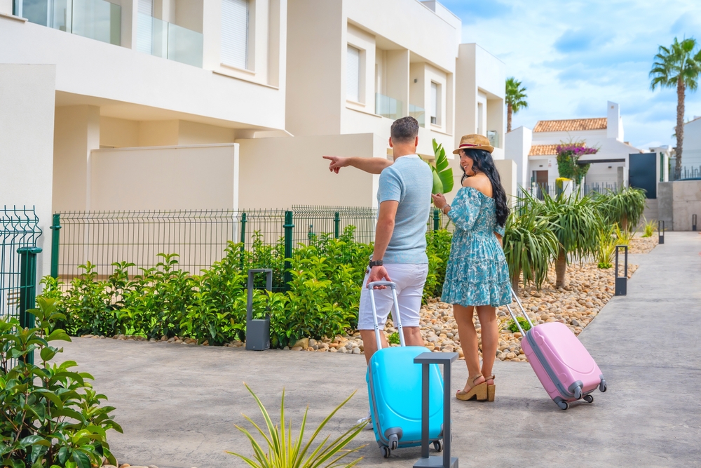 Image of vacationers with rolling suitcases pointing toward their rental