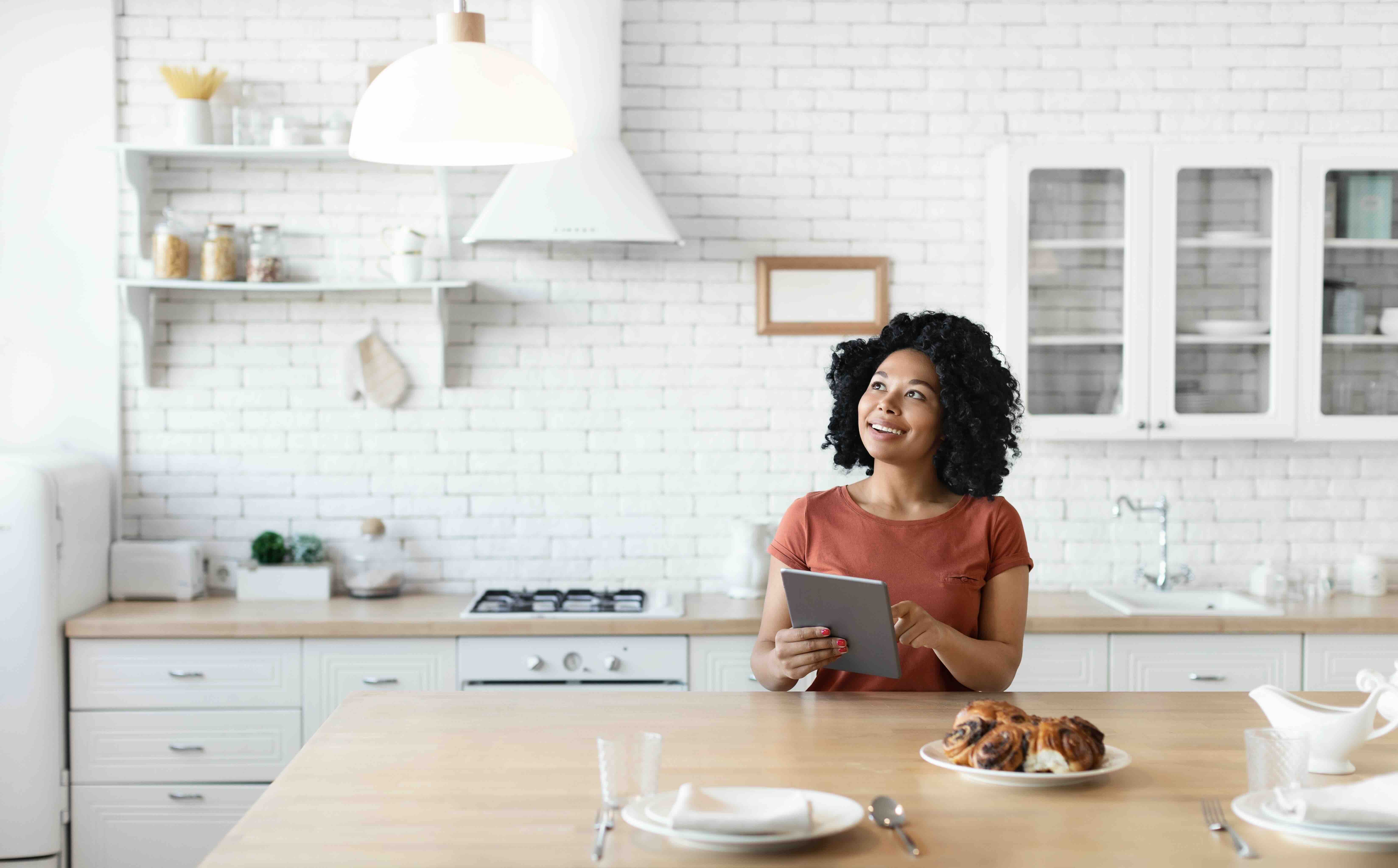 Woman controlling smart home from tablet in modern kitchen