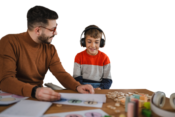 Image of man sitting at table with young boy who is wearing black headphones